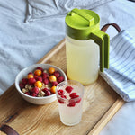 One Size Clear Fruit Infuser. In Takeya Pitcher on a tray next to a bowl of berries and a beverage with berries in it.